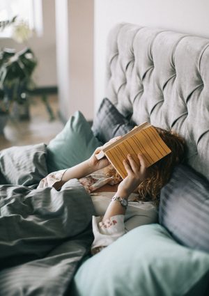 woman-covering-face-with-book-on-bed-1524232